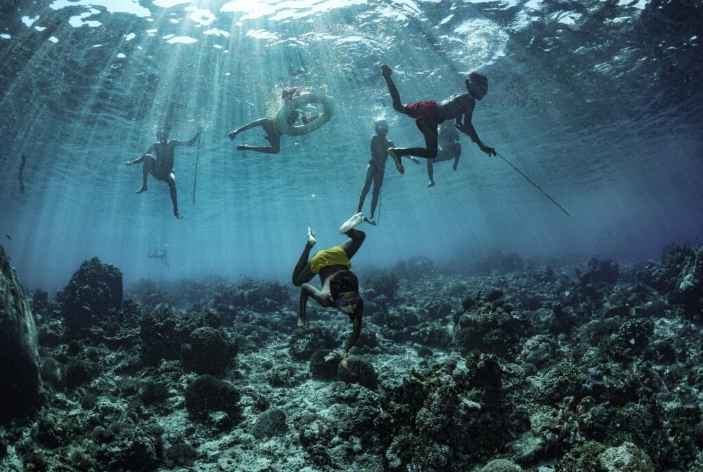 Divers explore coral reefs under sunrays in East Nusa Tenggara, Indonesia.