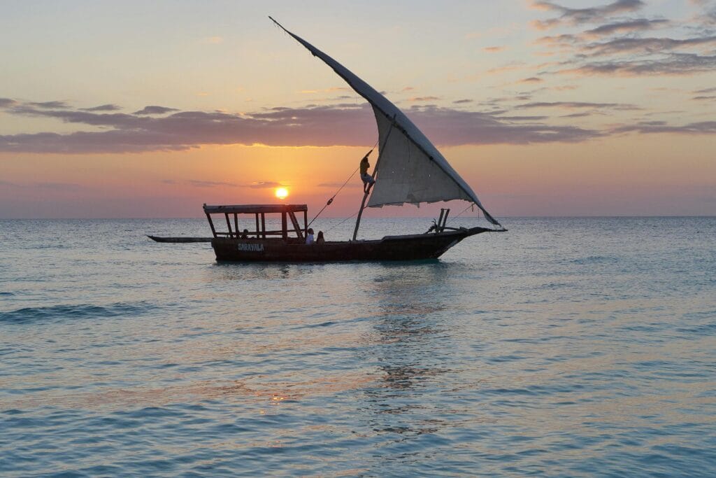 A dhow boat sailing during a stunning sunset over the Indian Ocean in Zanzibar, Tanzania.
