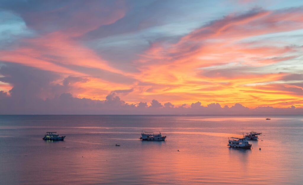 A tranquil sunset over a smooth sea with boats, creating a peaceful and idyllic seascape.