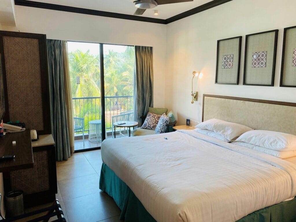 Cozy hotel bedroom with balcony overlooking lush palm trees, offering a relaxing tropical escape.