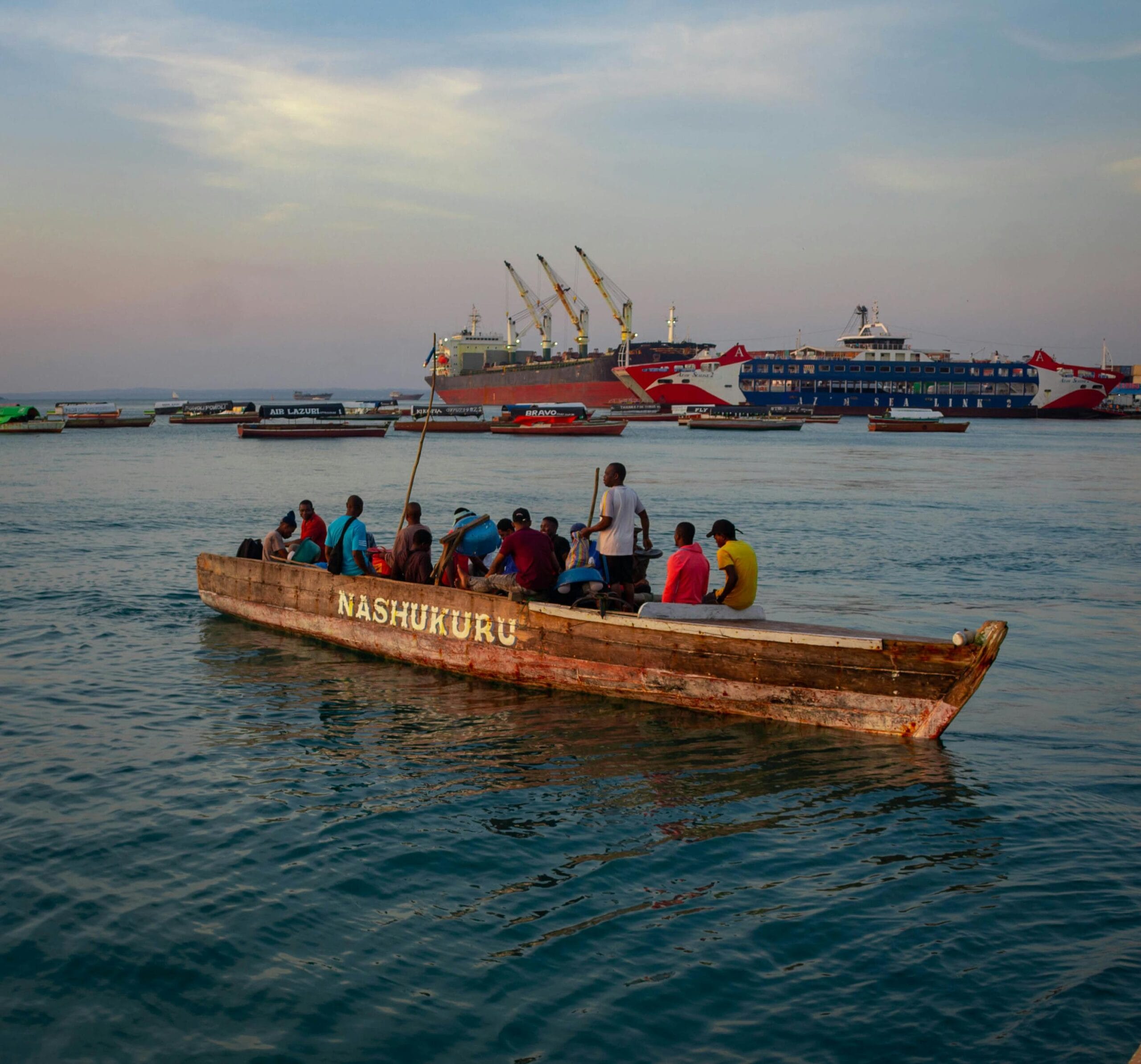 How to get to Zanzibar from Dar es Salaam 2 A group of people on a traditional wooden boat in Zanzibar at sunset, with ships in the background.