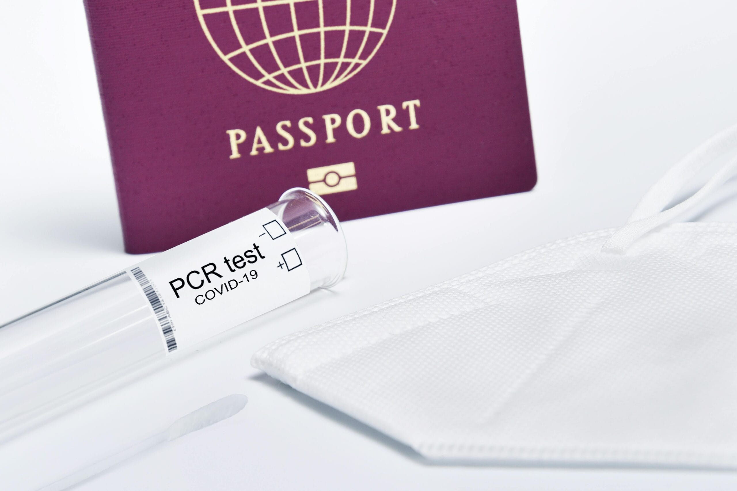 Close-up of a passport, KN95 mask, and PCR test kit highlighting travel safety measures.