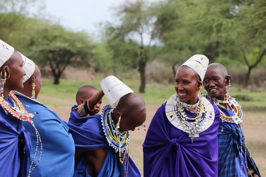 A group of Maasai women and a child in traditional attire sharing joyful moments in Tanzania.