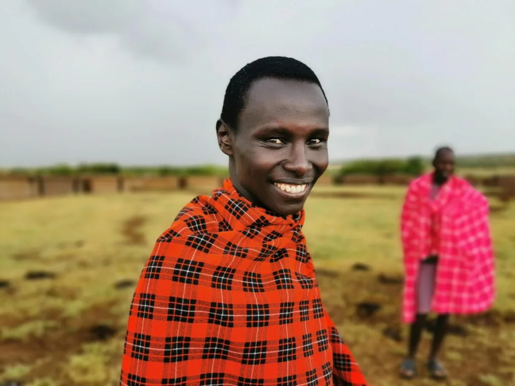 Portrait of a smiling man in Maasai attire outdoors in Kenya, showcasing cultural richness.