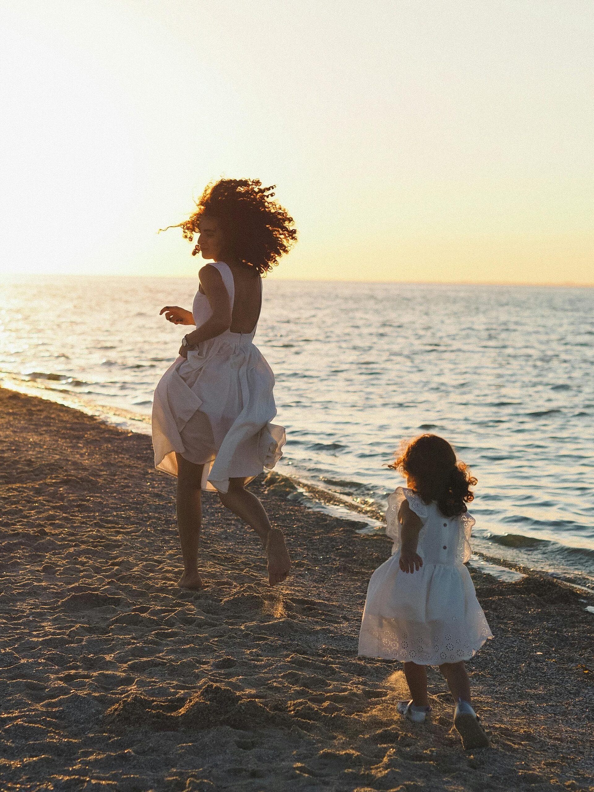 Best practices for traveling with children in Zanzibar 1 Heartwarming scene of a mother and daughter running along the beach at sunset in white dresses.