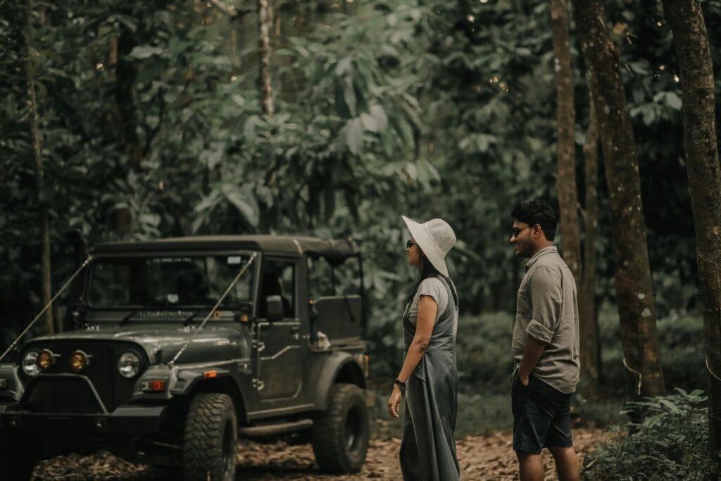 Stylish couple walking near a rugged jeep in a lush tropical forest.
