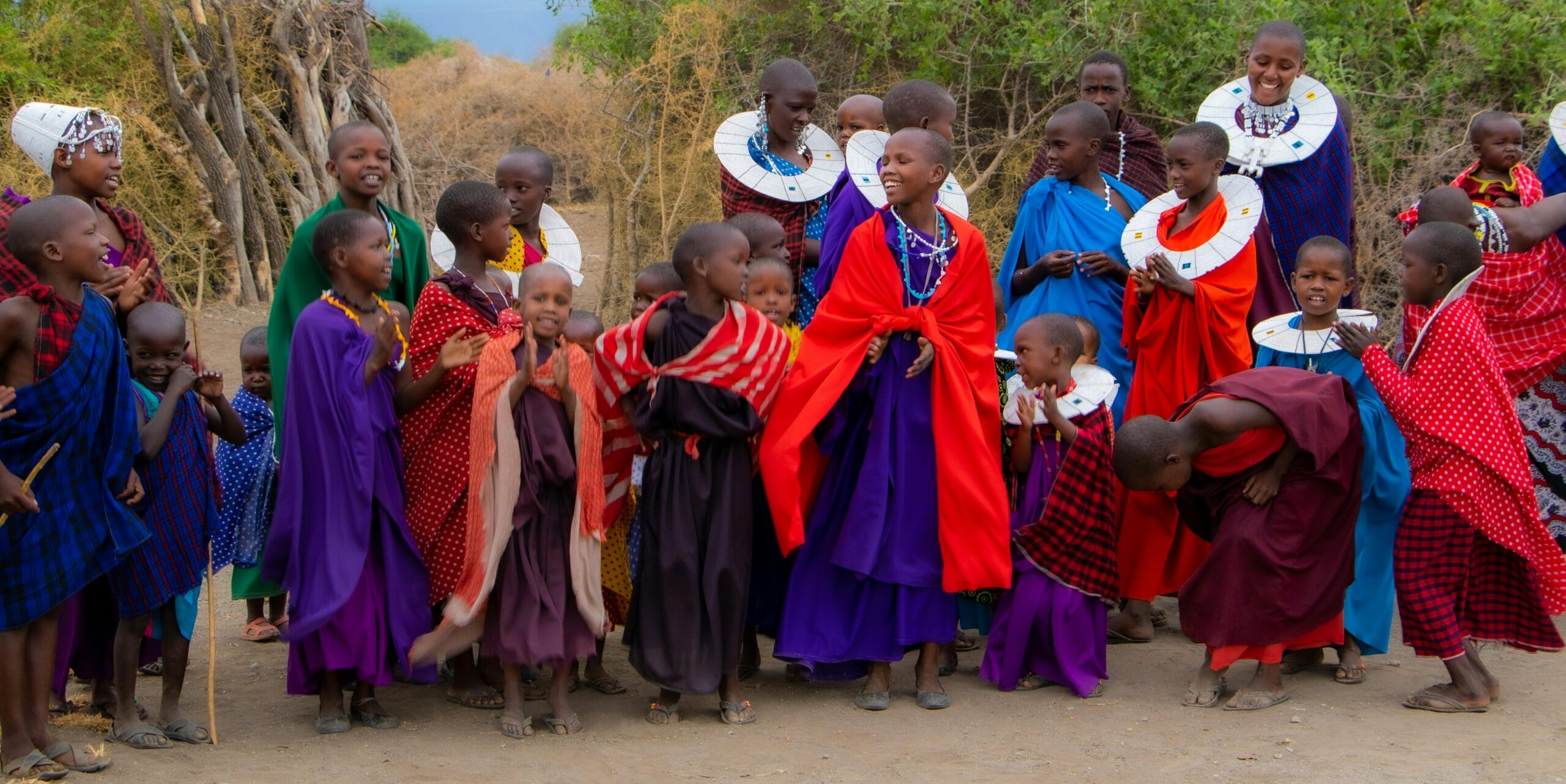 Group of Maasai children in vibrant traditional clothing dancing outdoors, showcasing cultural celebration.