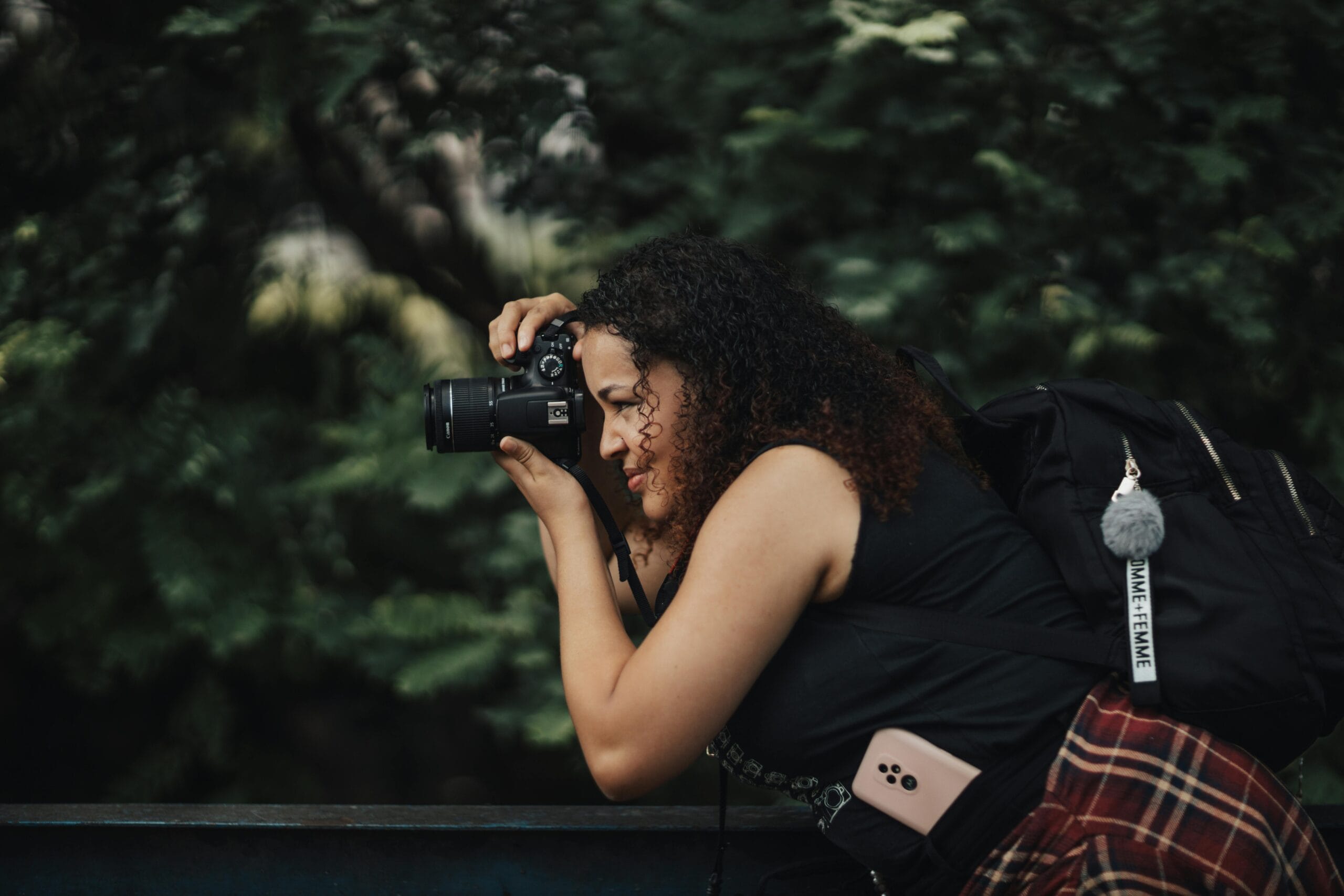 A woman with a camera takes photos in a lush green outdoor setting.