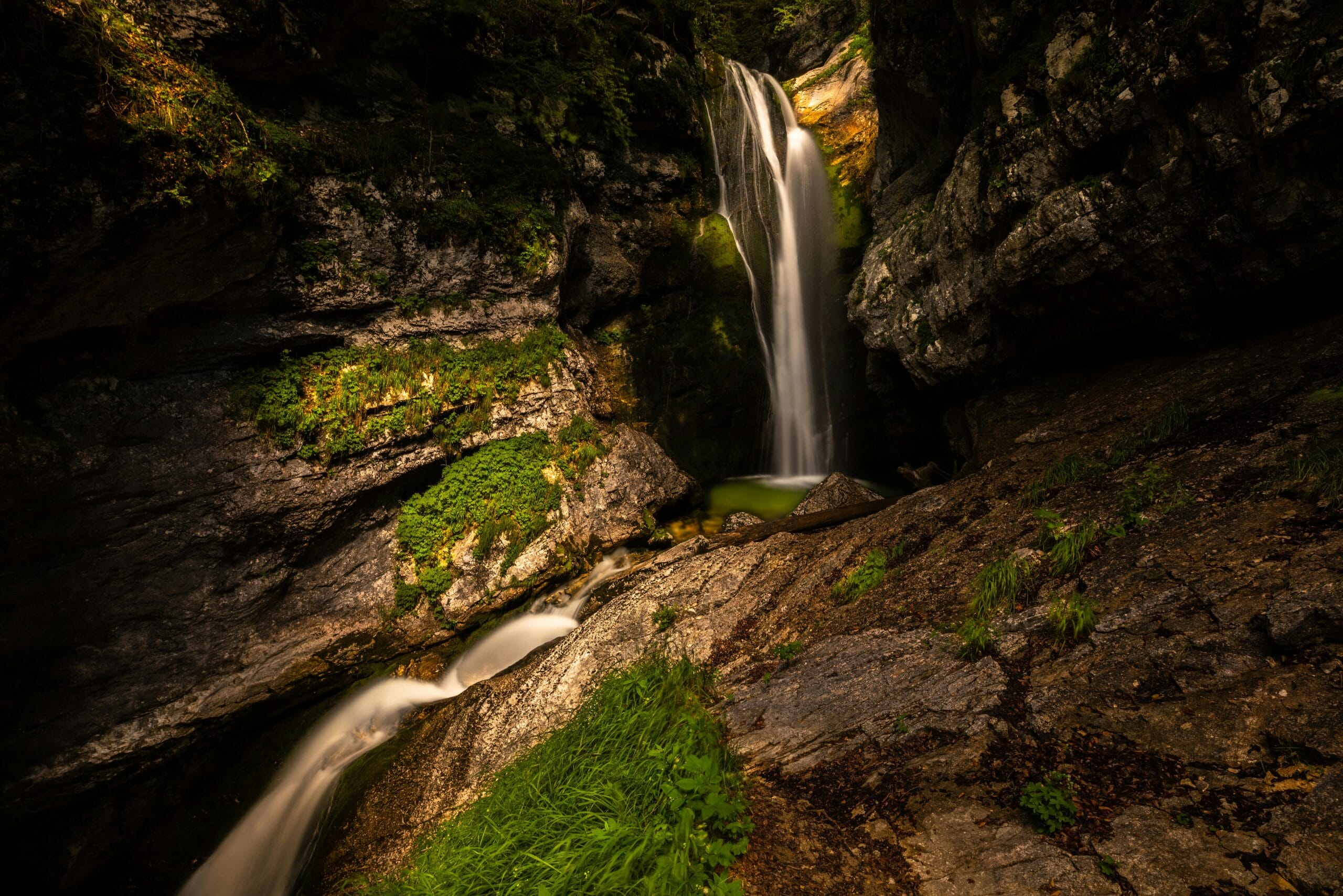 A stunning waterfall cascading into a clear creek amid lush greenery in Stara Fužina, Slovenia.