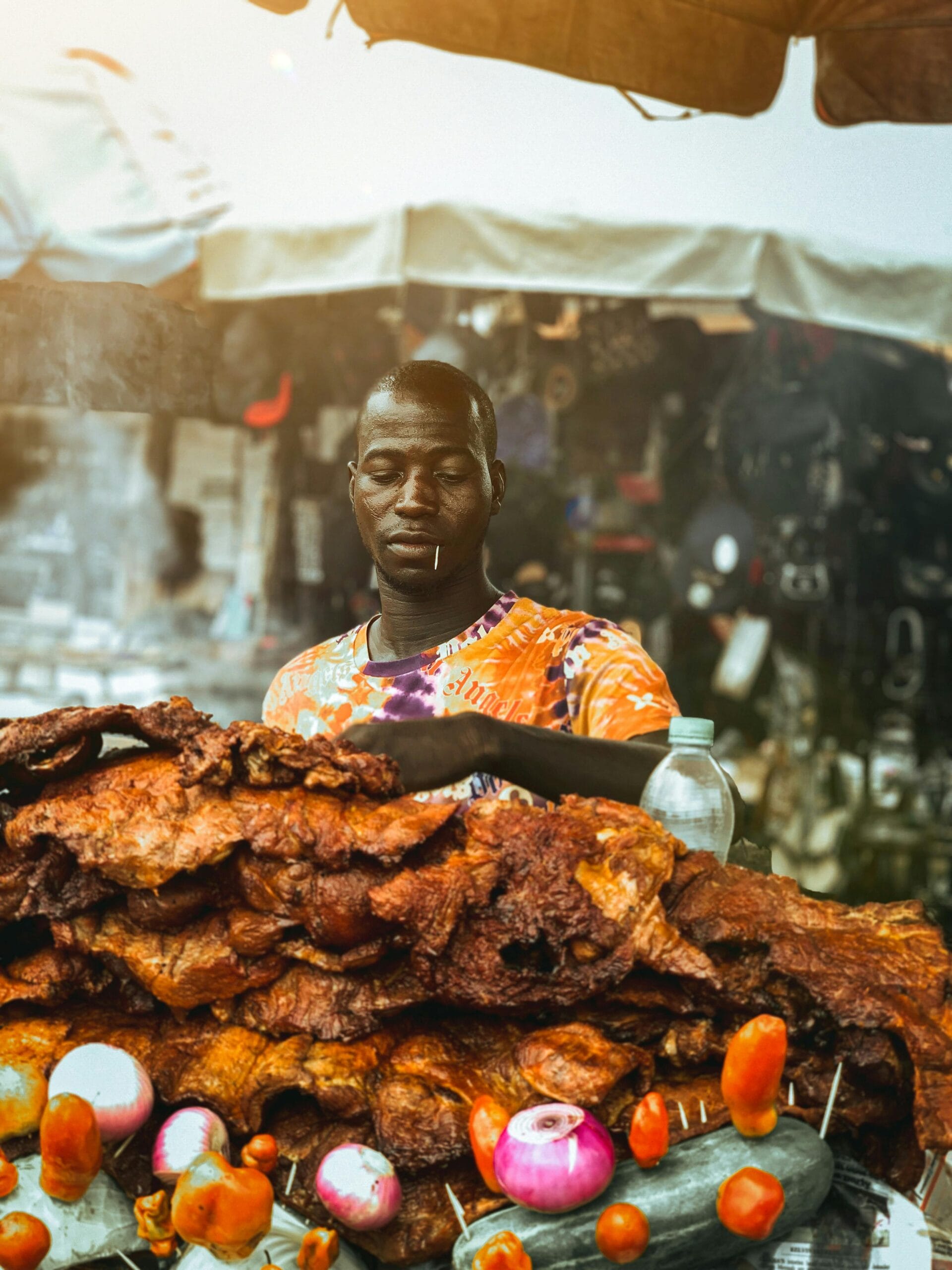 Tanzanian Cooking Classes on Safari: A Culinary Adventure in the Heart of Africa 2 Man grilling meat at street stall with colorful vegetables in a bustling market.