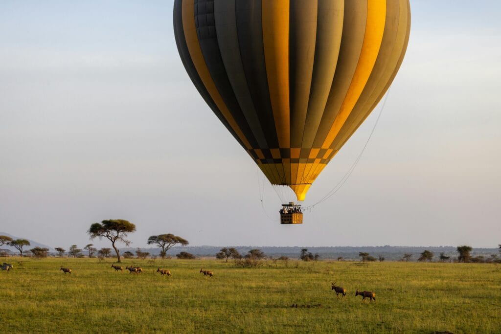 Majestic hot air balloon floats over African savannah with antelopes below.