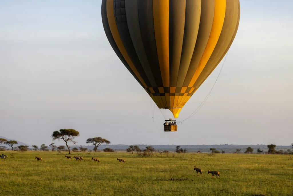Majestic hot air balloon floats over African savannah with antelopes below.