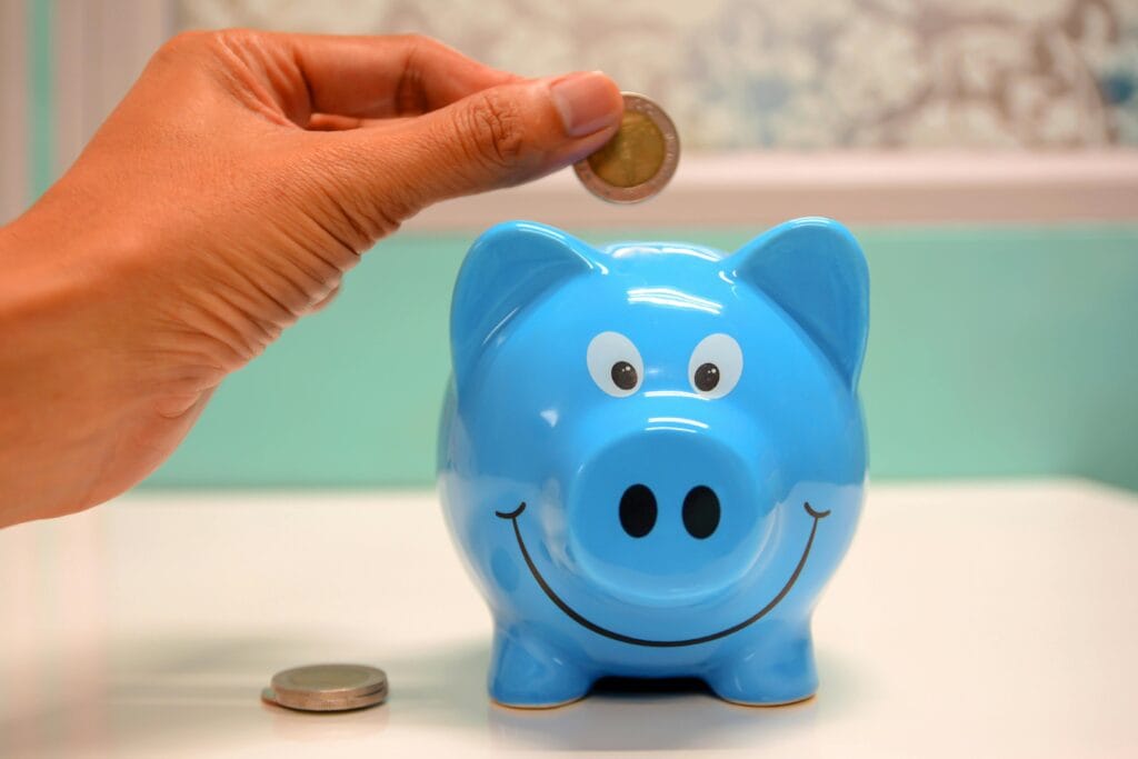 How to Save Money on African Safaris 1 Hand inserting a coin into a blue piggy bank for savings and money management.