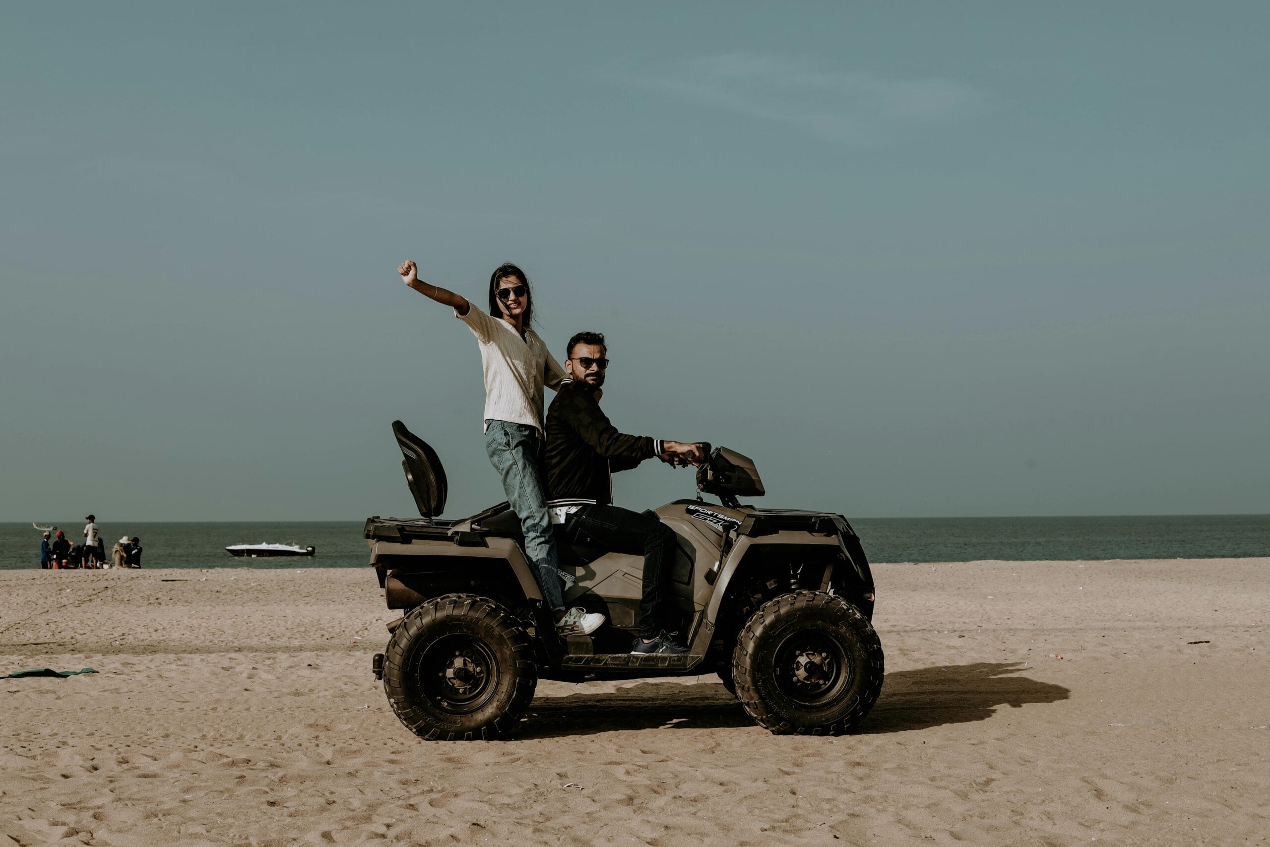 A couple enjoying a ride on a quad bike along a picturesque sandy beach with a clear sky overhead.