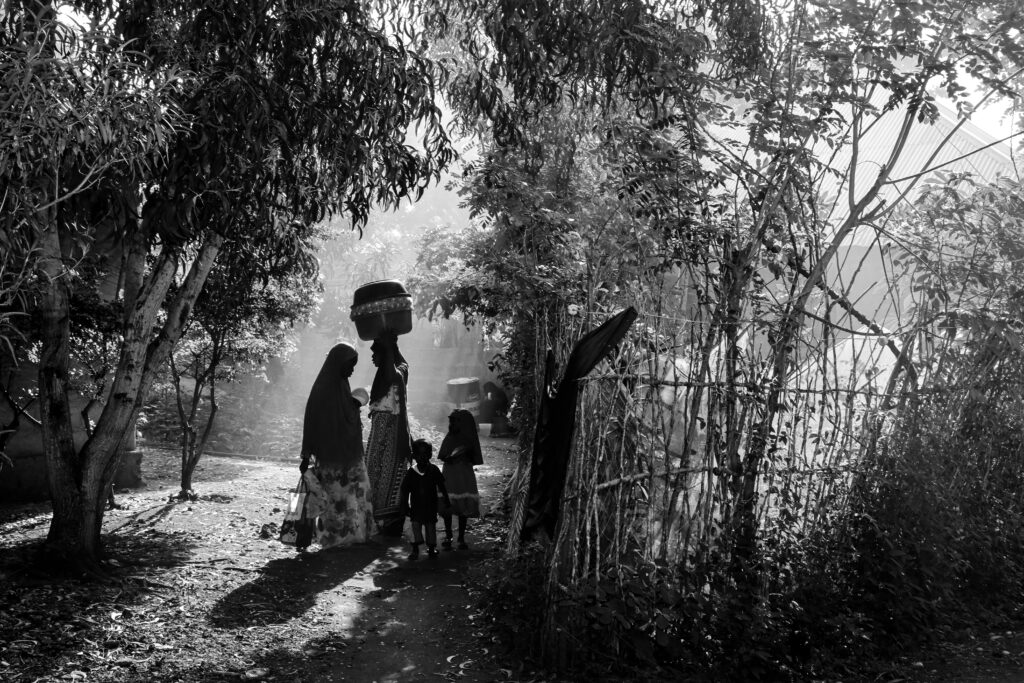 Cultural excursions in Zanzibar 13 Silhouetted figures of women and children walking under sunlight in a village pathway surrounded by trees.