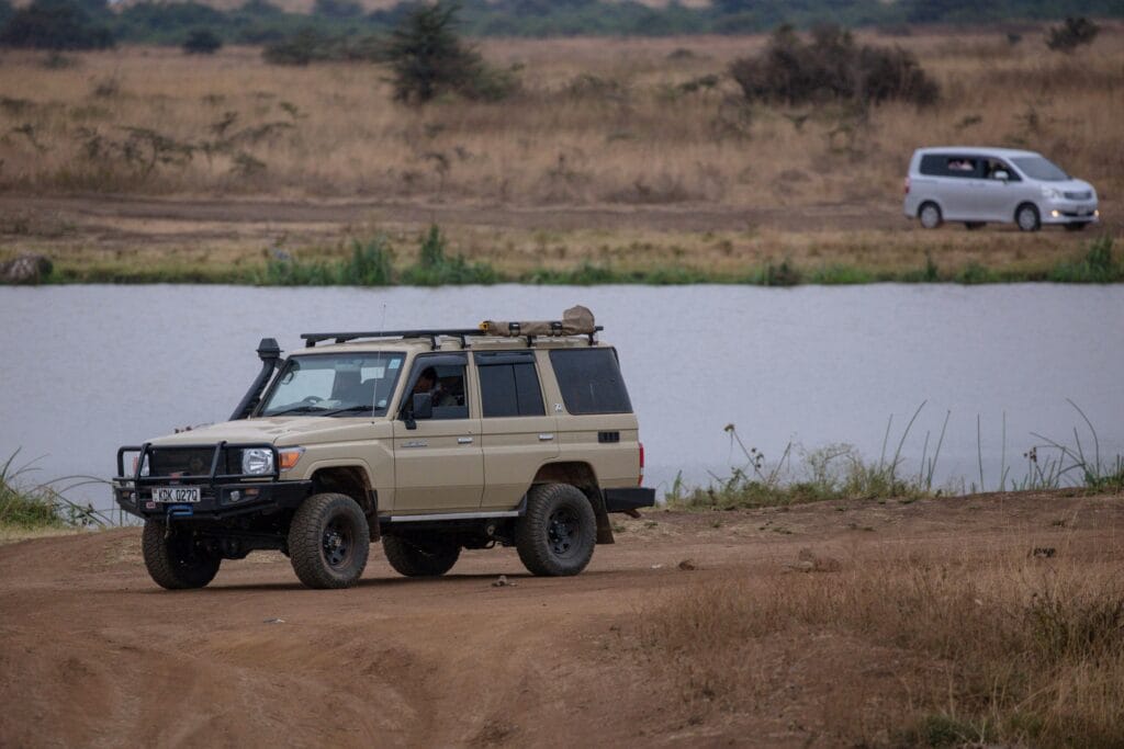 A safari vehicle parked by a serene lake in a vast African savanna landscape.