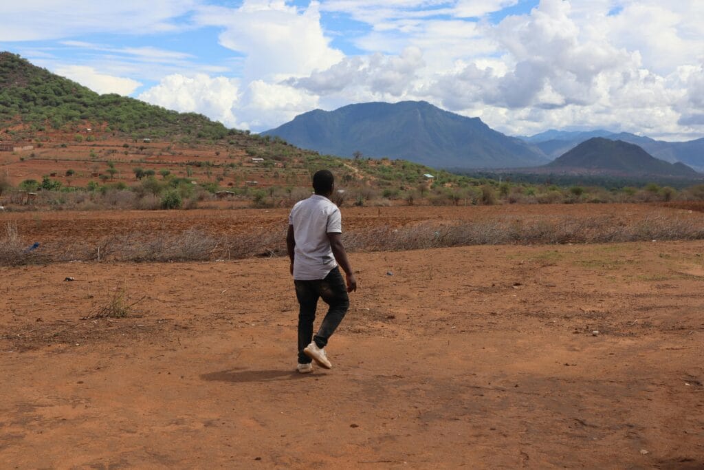 What to Expect on a Walking Safari 7 A man walks on the dry, scenic landscape of Taveta, Kenya with lush mountains.