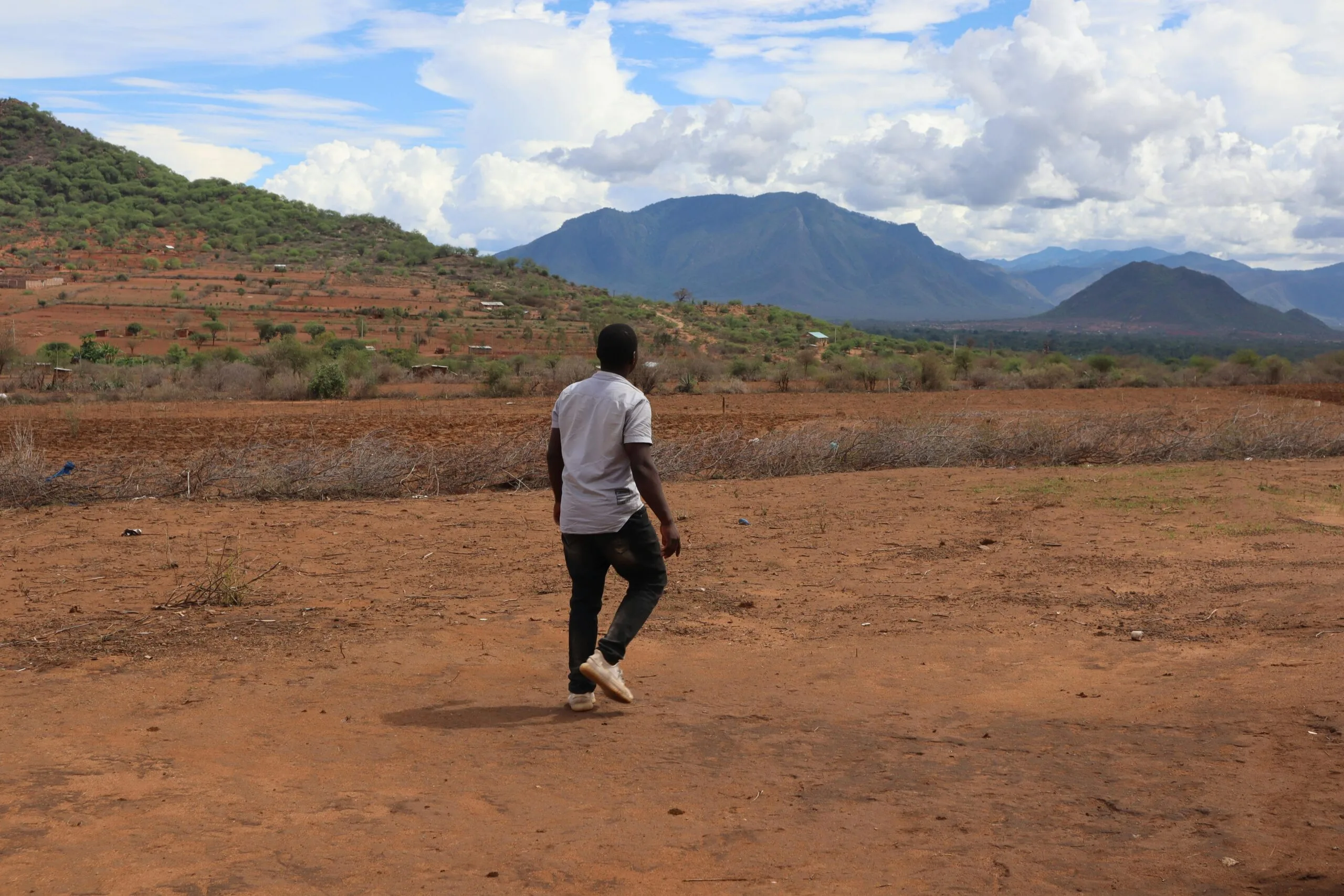 A man walks on the dry, scenic landscape of Taveta, Kenya with lush mountains.