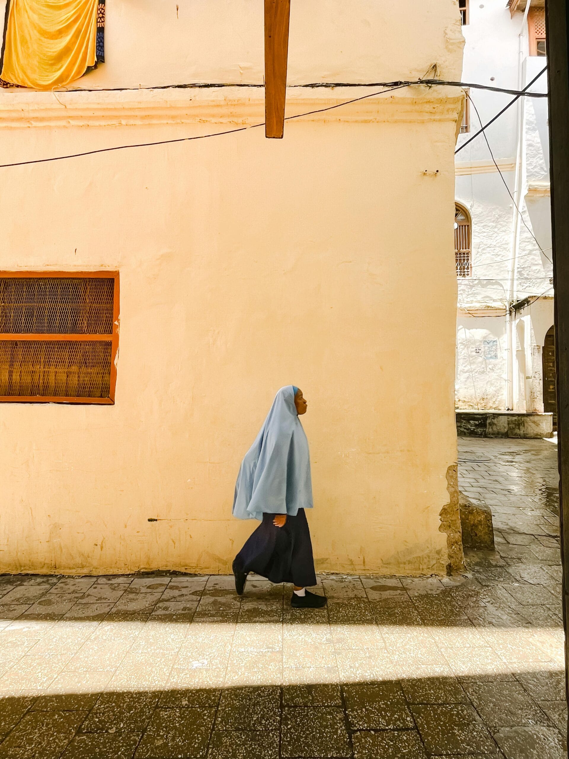 Stone Town walking tours 1 A woman in traditional clothing walks along a sunlit street in Zanzibar, Tanzania.