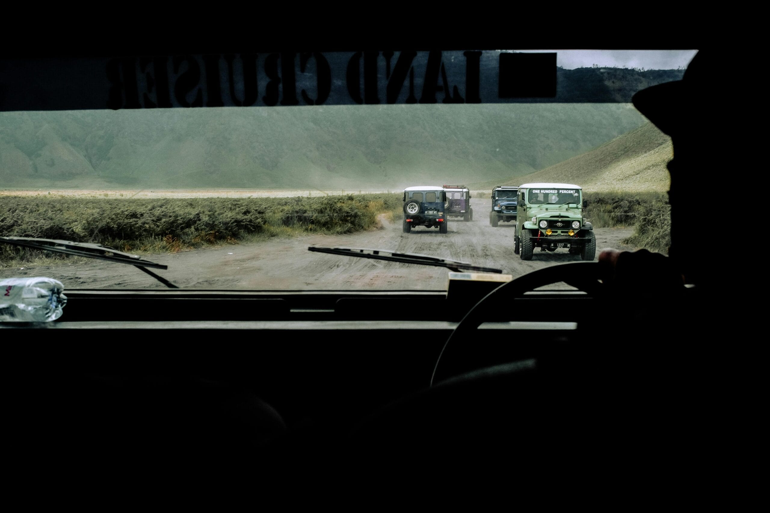 Scenic off-road journey with multiple Land Cruisers on a dirt road, viewed from a windshield perspective.