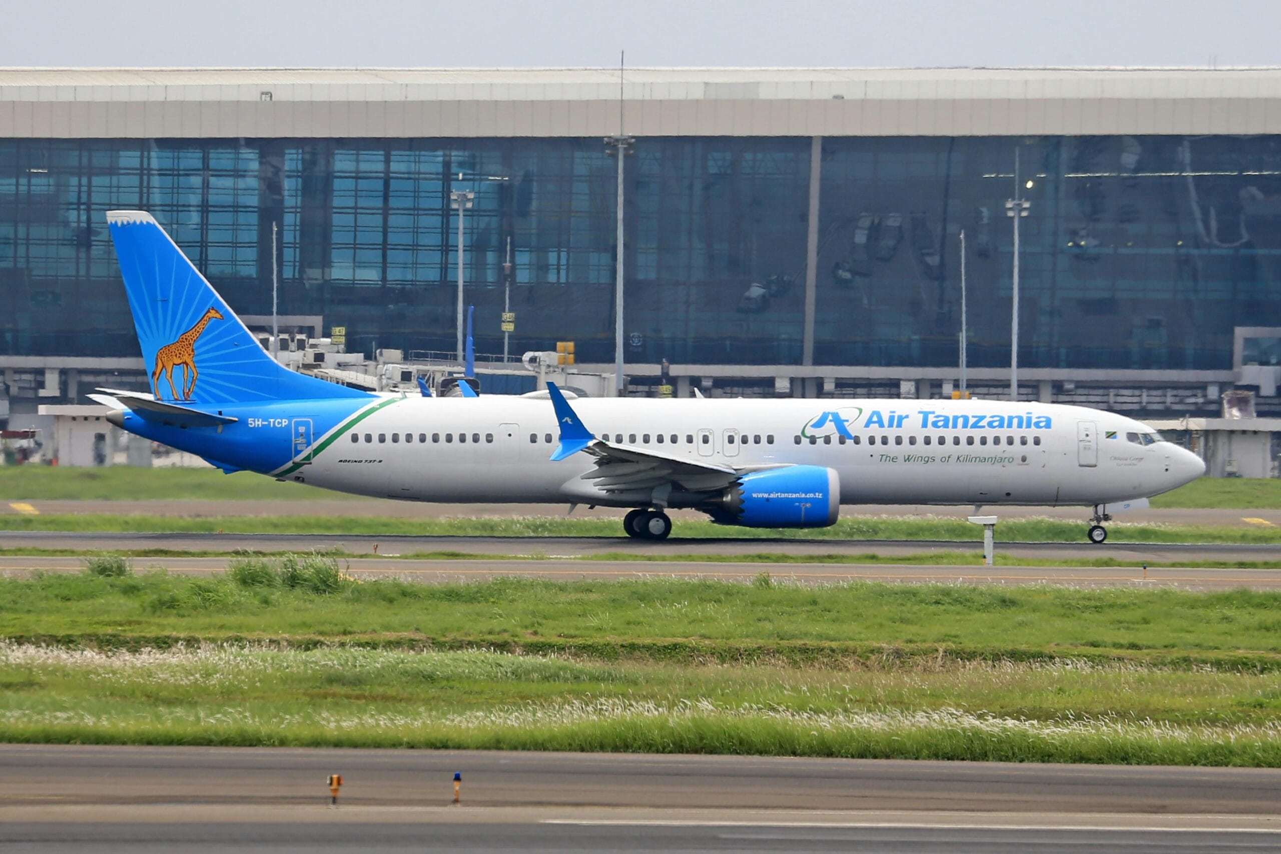 Air Tanzania passenger plane taxiing at a contemporary airport terminal on a sunny day.