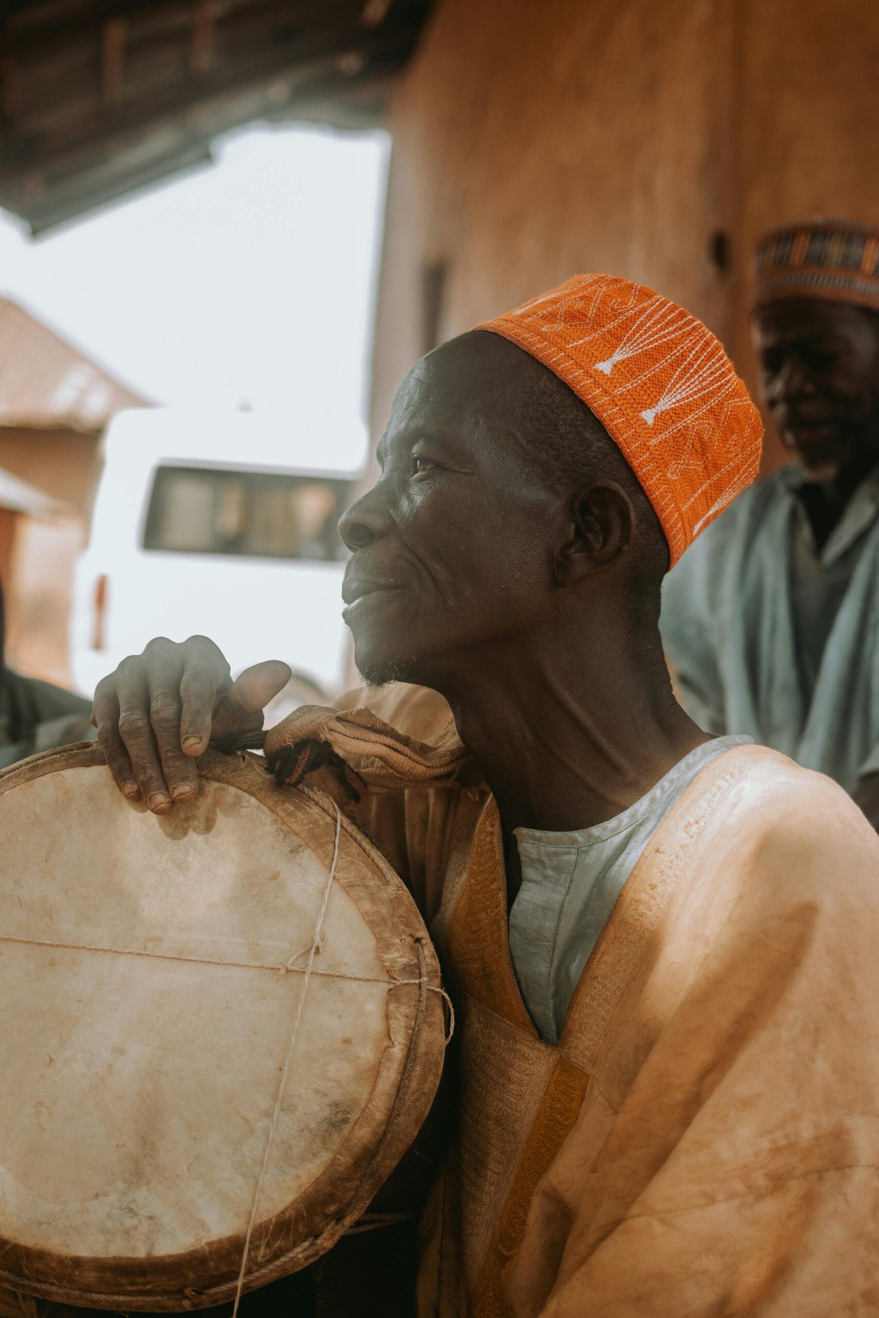 How to enjoy traditional Zanzibari music 1 Elderly Nigerian man in traditional attire playing a drum outdoors in Essan.