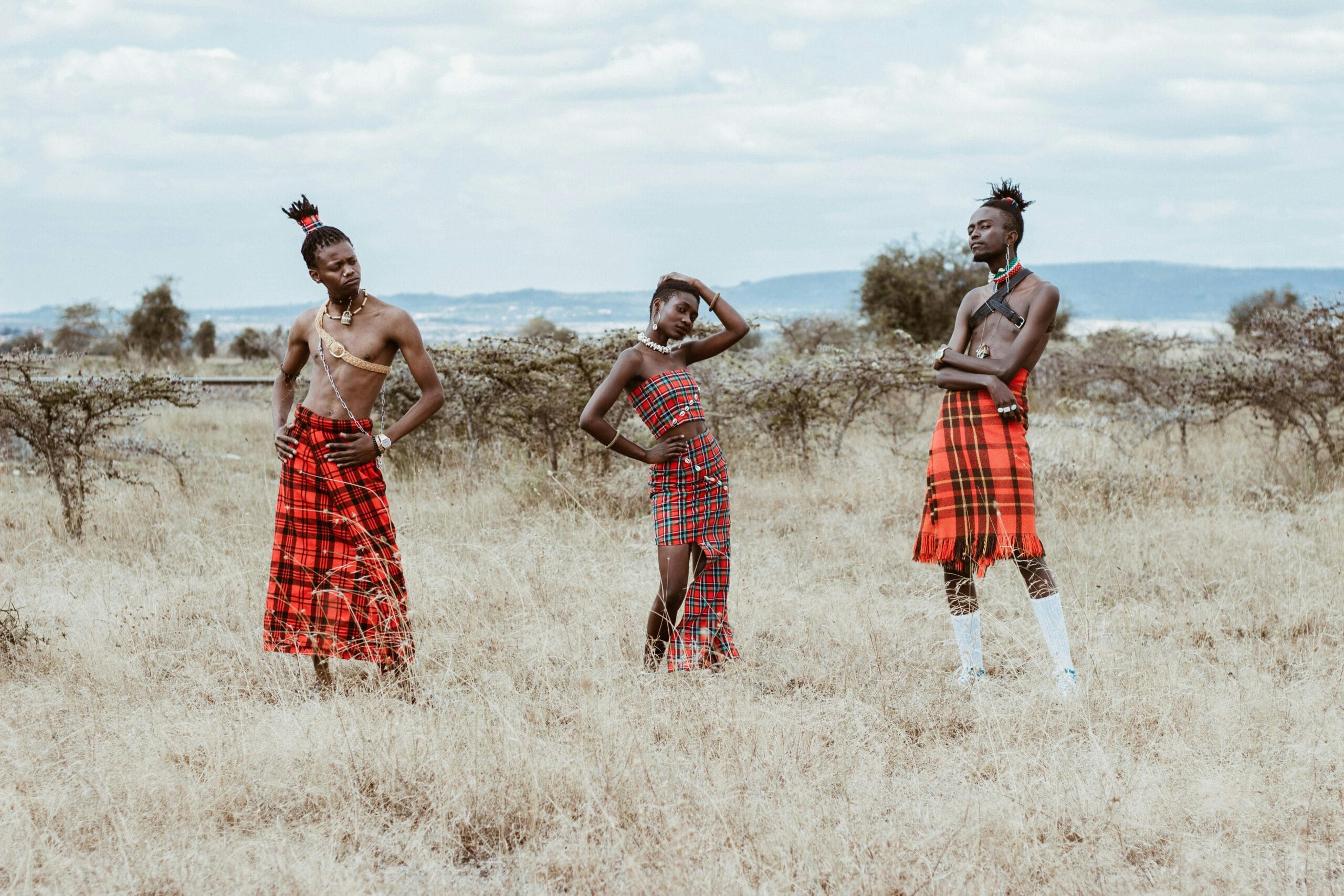 Three people in traditional tribal attire posing in a vast African grassland.