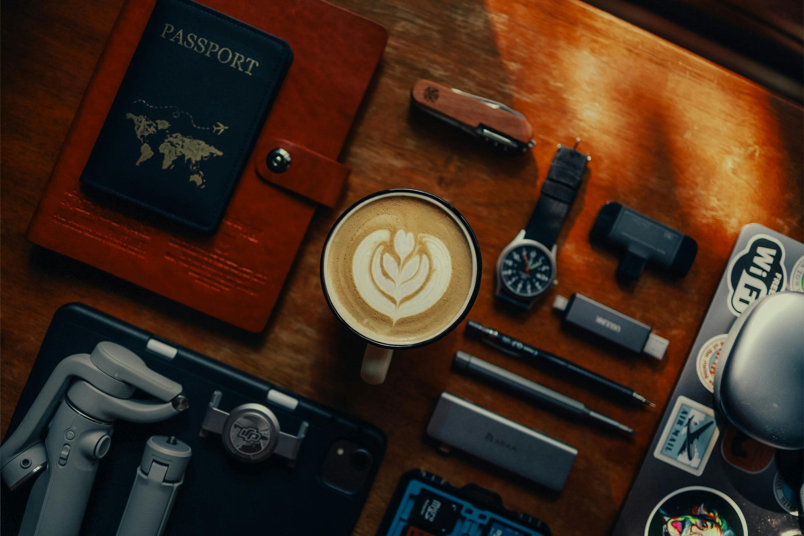Flat lay of travel essentials with coffee, gadgets, and a passport on a wooden table.