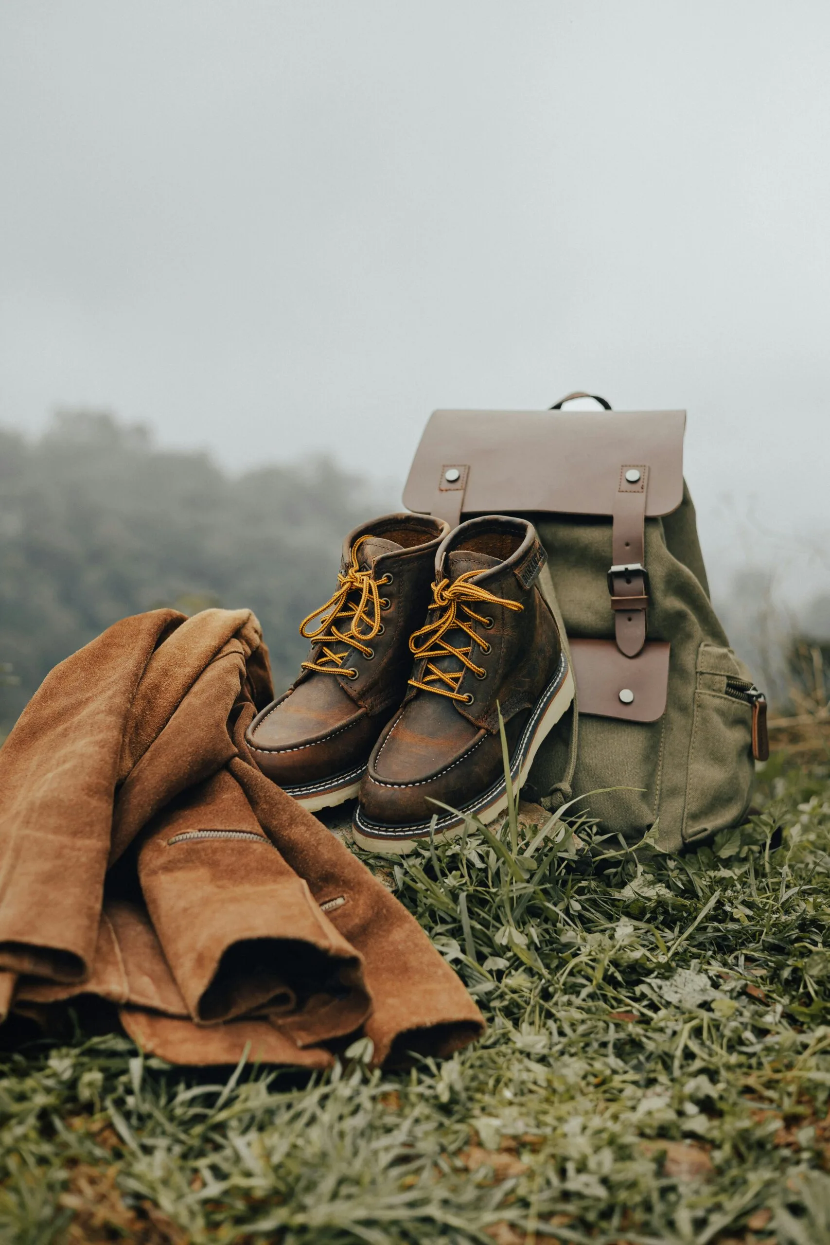 Vintage boots, jacket, and backpack in a misty mountain landscape.