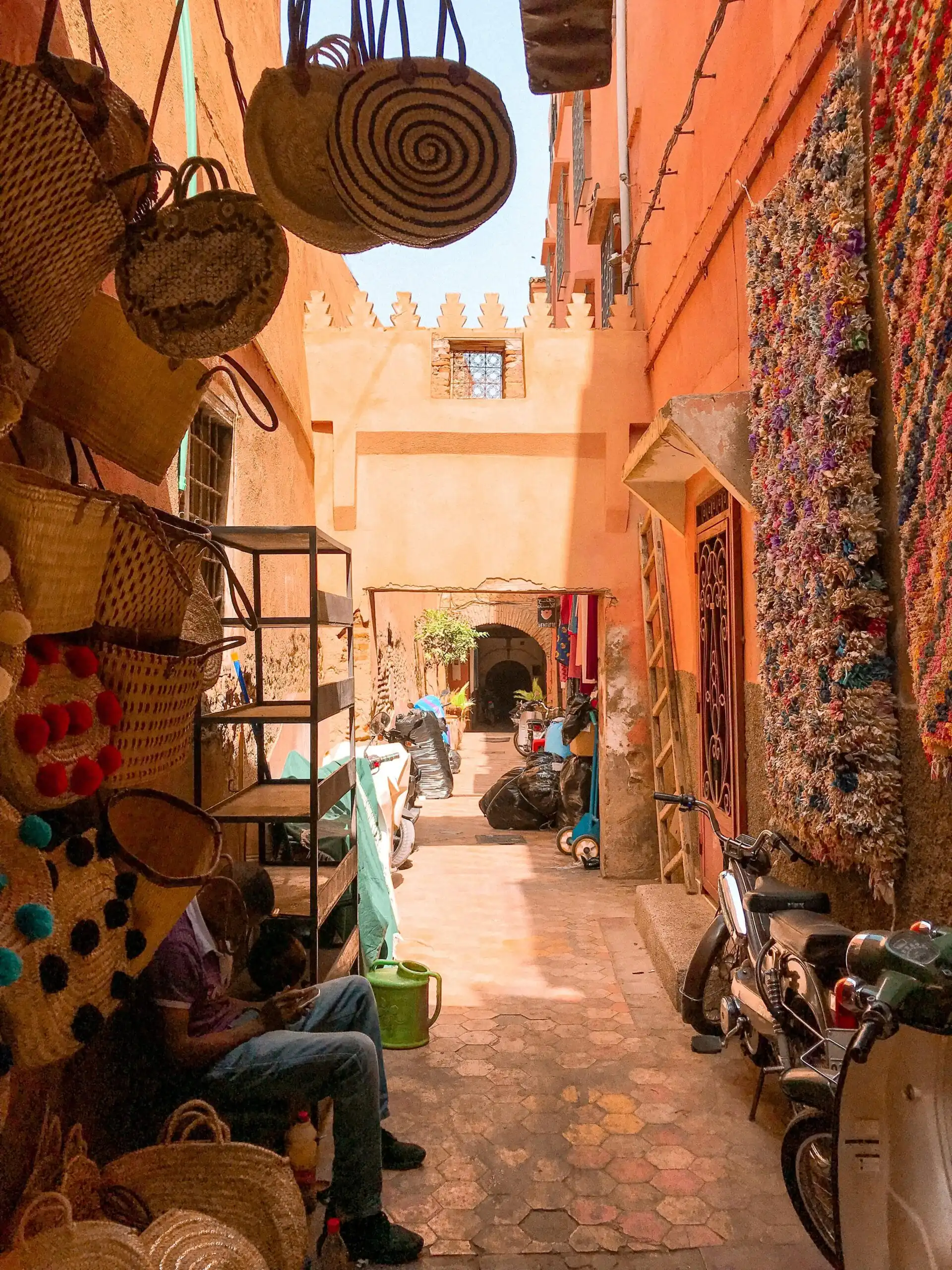Shopping for Local Crafts in Zanzibar: Where to Find Unique Souvenirs 1 Colorful alley in Moroccan bazaar with shops, woven baskets, and motorbikes under daylight.