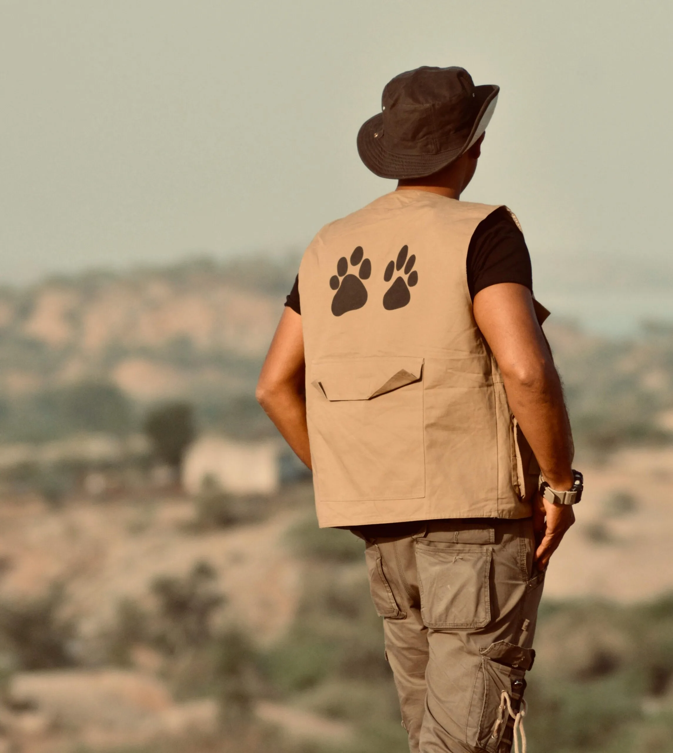 Back view of a man in a safari vest and hat gazing at a desert landscape.