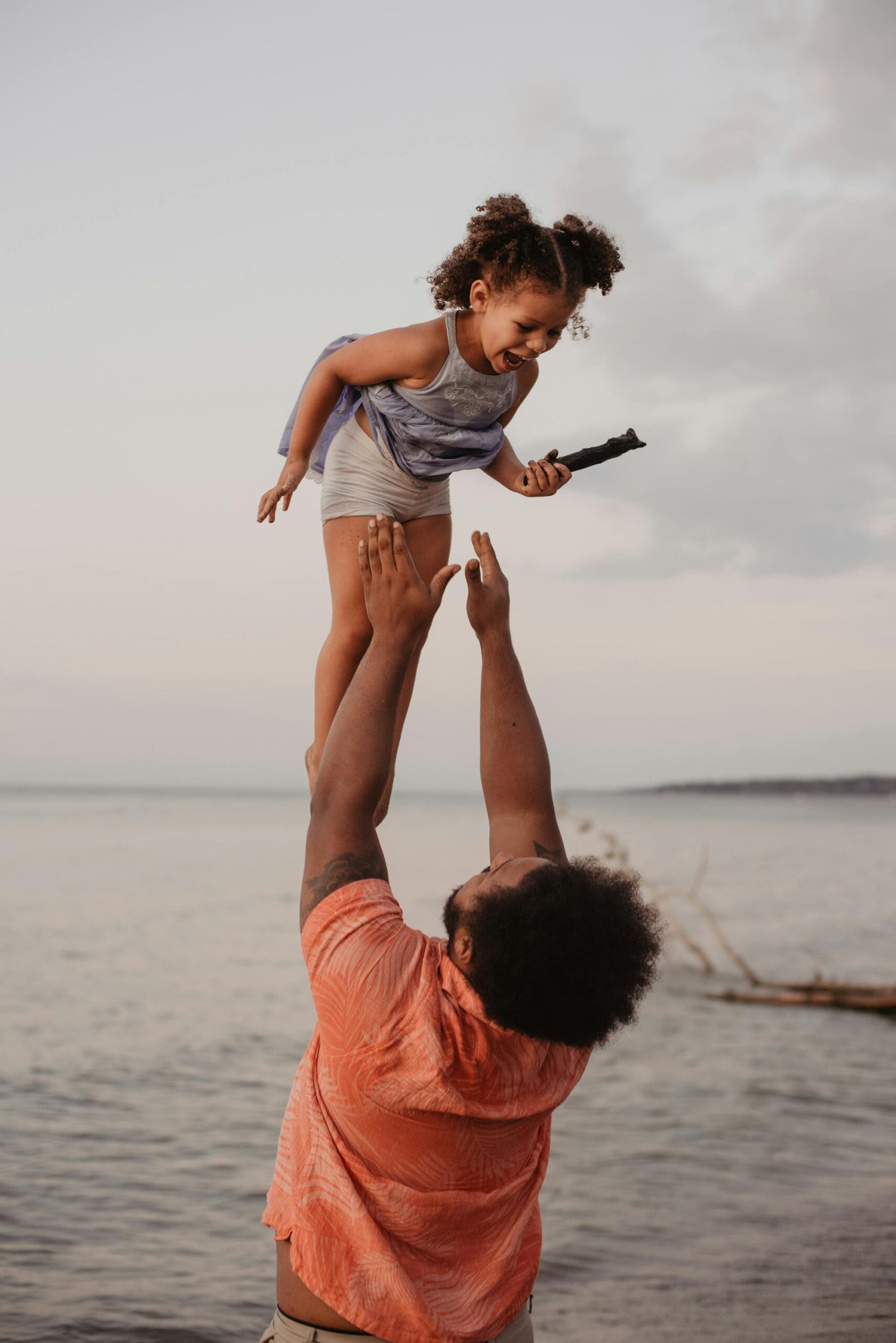 Best practices for traveling with children in Zanzibar 2 A joyful father lifts his daughter in the air by the beach during sunset, capturing a moment of love and happiness.