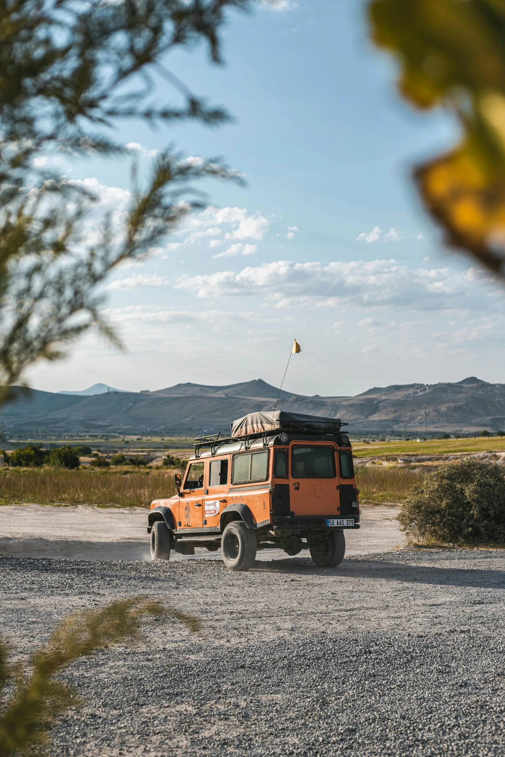 Orange jeep driving through scenic countryside on a sunny day, ideal for adventure or travel themes.