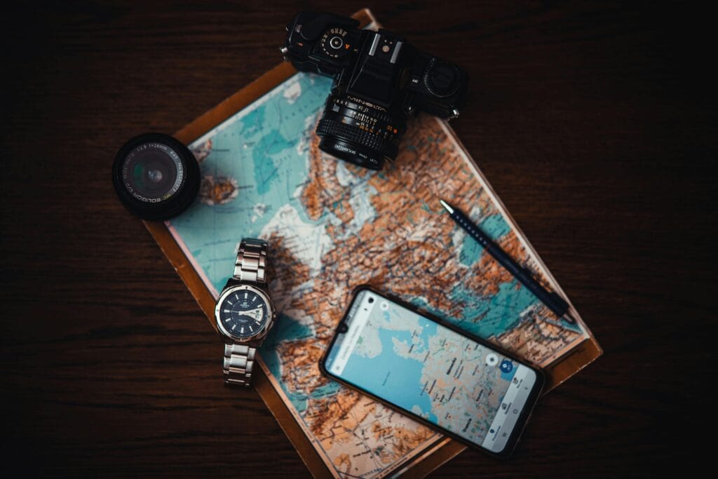 Planning a multi-destination trip including Zanzibar 7 Top view of travel essentials including a map, camera, phone, watch, and lens on a wooden surface.