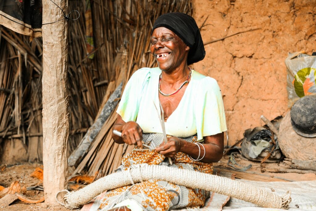 Supporting Local Crafts in Tanzania: A Journey Through Art, Culture, and Community 22 An African woman smiles as she weaves in a rural Tanzanian setting, showcasing traditional craftsmanship.