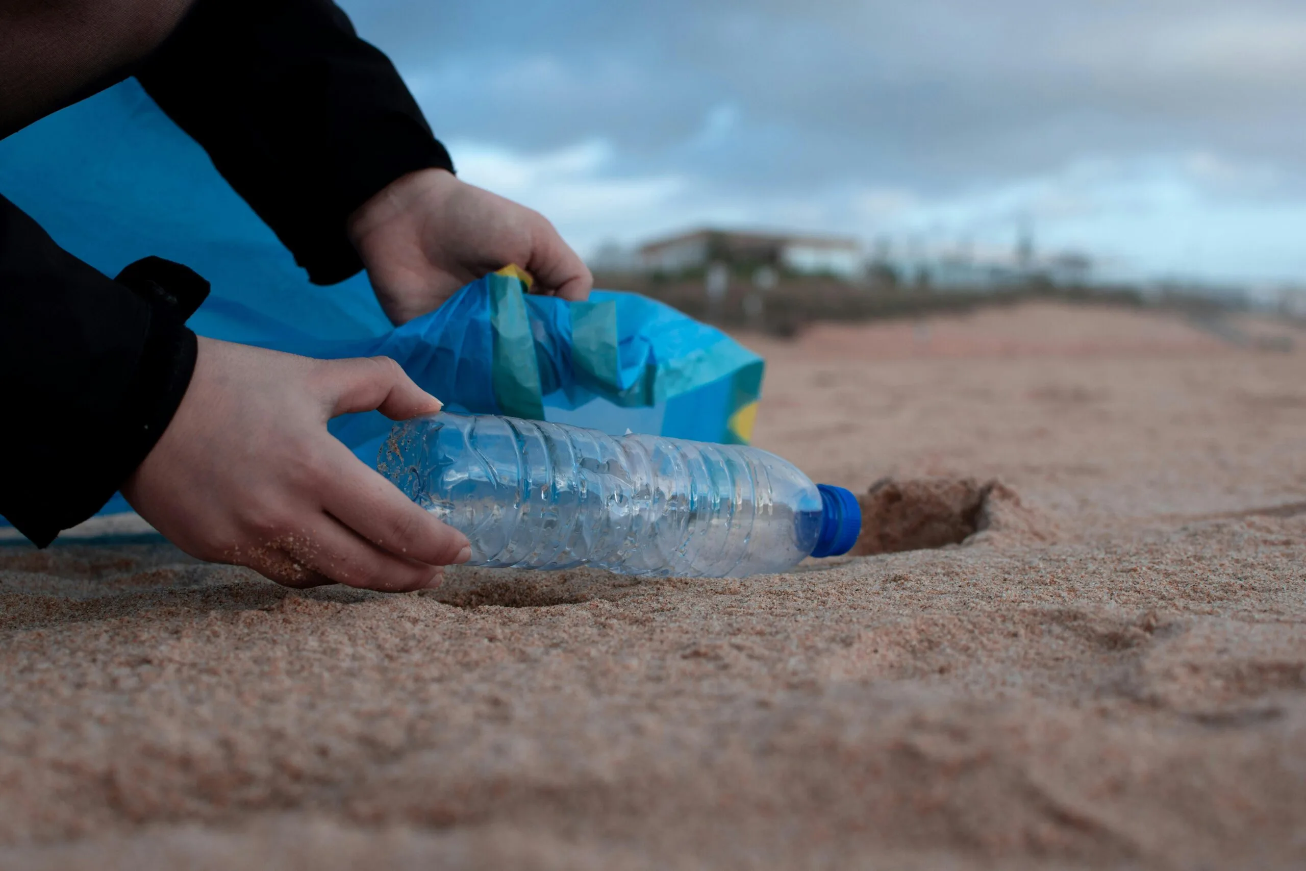How to volunteer in Zanzibar 2 Hands collecting a plastic water bottle from the sandy beach, promoting environmental awareness.