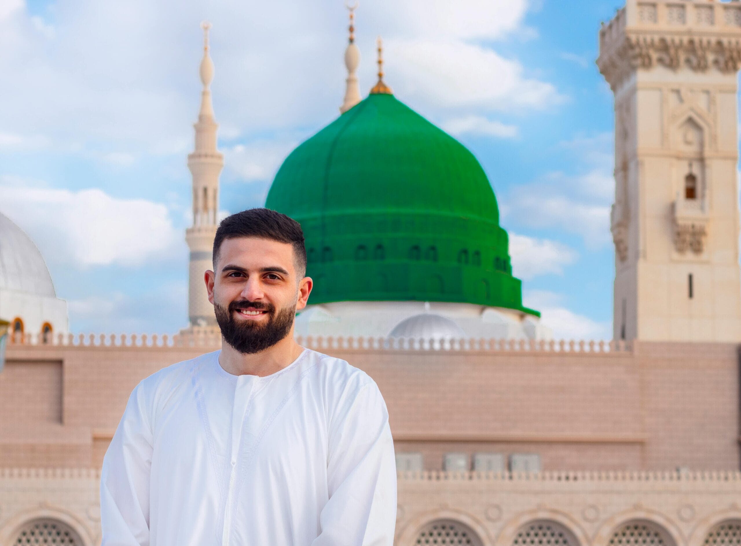 A bearded man smiling in front of the iconic green dome of Al-Masjid an-Nabawi, Medina.