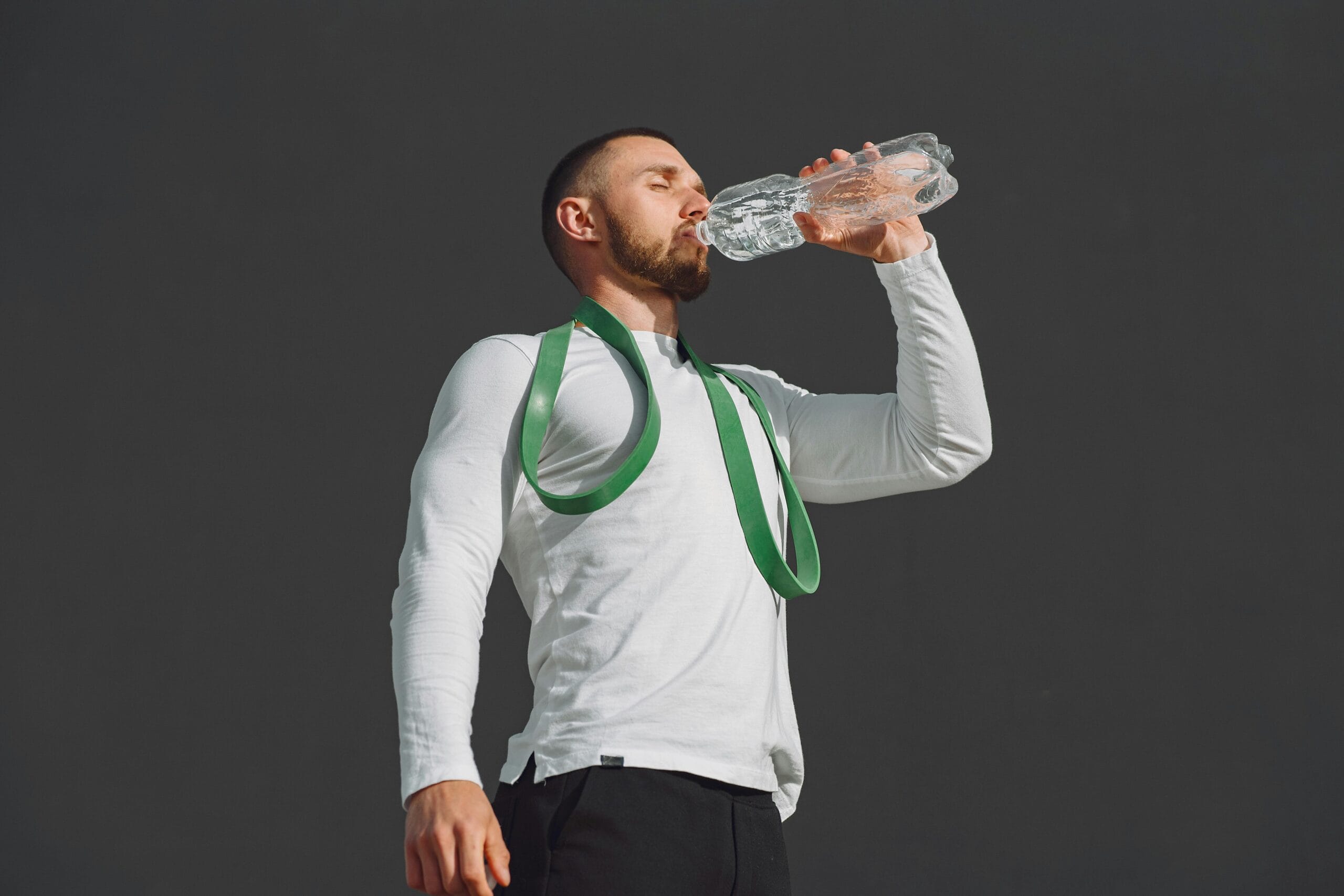 Athletic man in sportswear drinking water outdoors, promoting hydration.