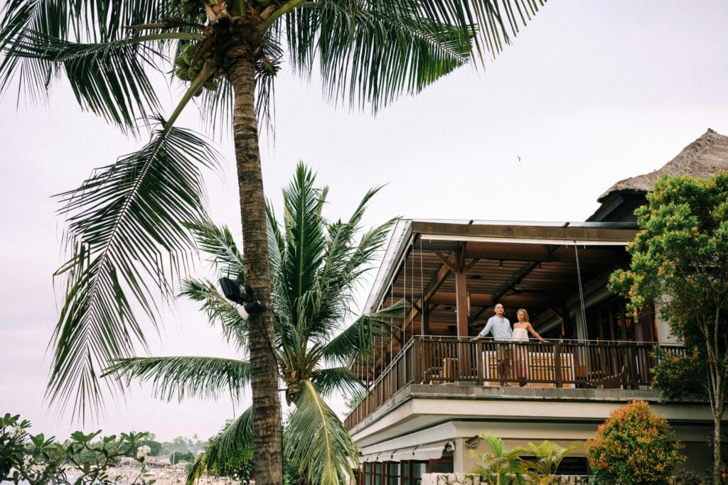 7-Day Safari and Zanzibar Luxury Escape for Honeymooners: A Perfect Romantic Getaway 19 A couple enjoys a peaceful moment on a luxury resort balcony surrounded by palm trees.