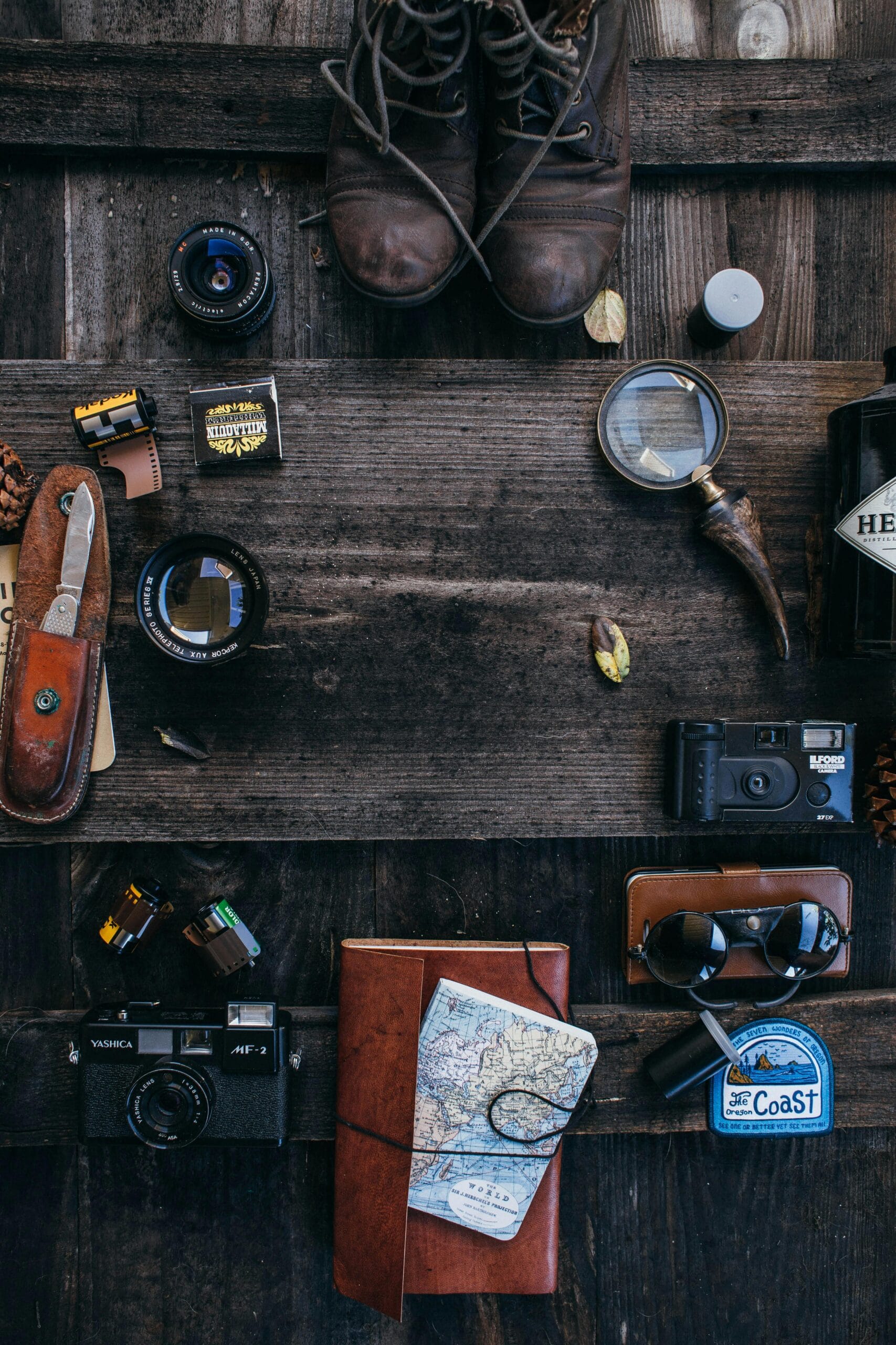 Must-have safari gadgets and gear 1 Flat lay of vintage travel essentials including cameras, map, and boots on a rustic wooden surface.
