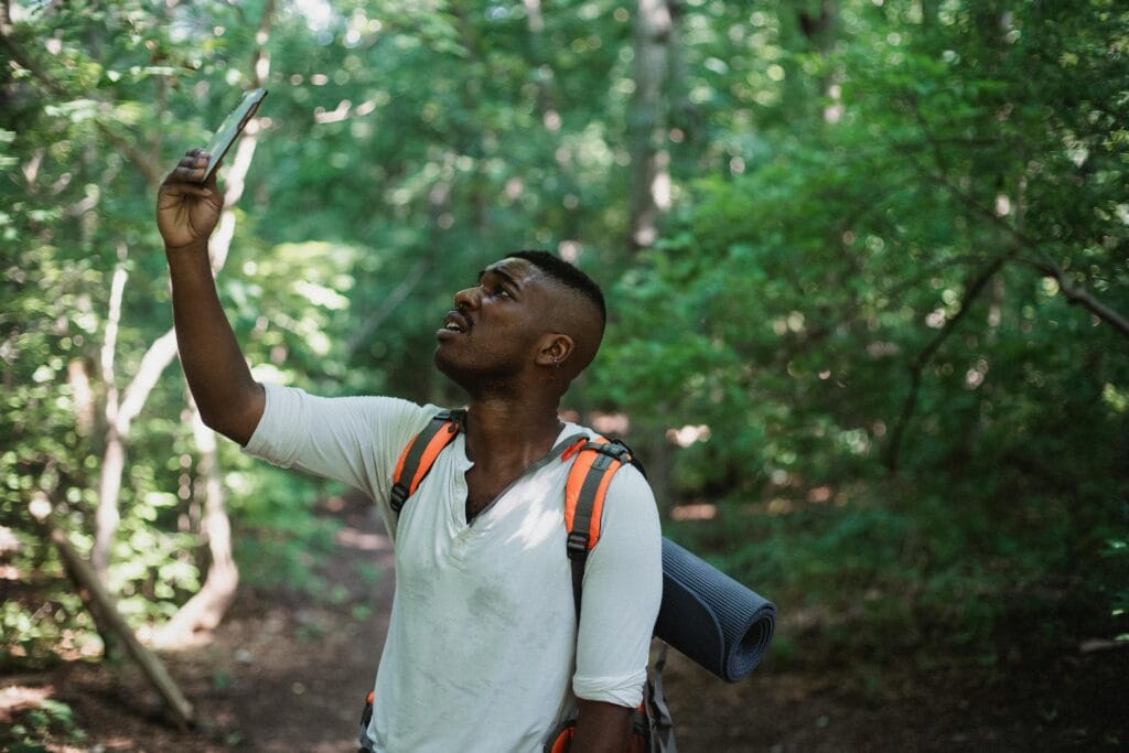 Emergency contacts for safaris 11 African American male with backpack standing in forest and holding mobile phone while catching GPS signal during hike