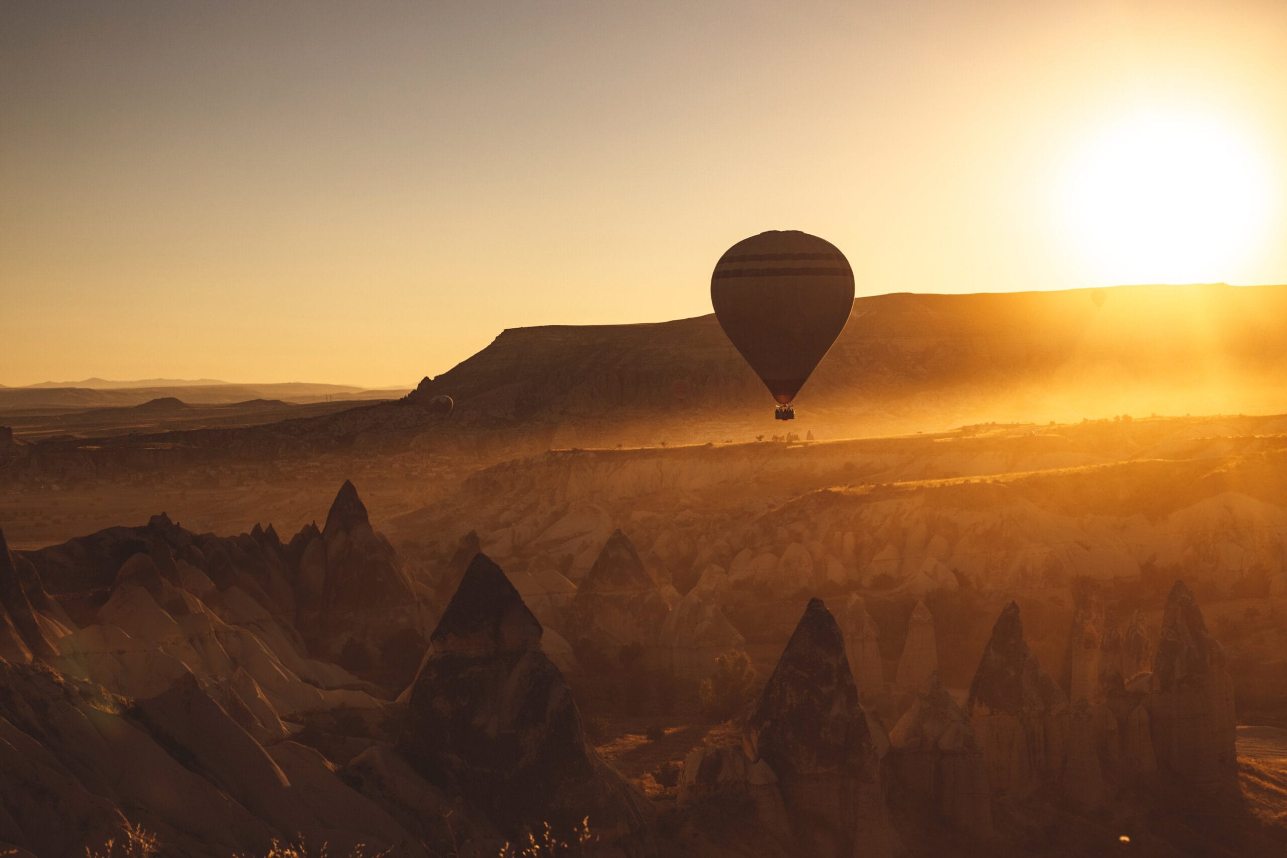 A hot air balloon floats over the stunning rock formations of Cappadocia during a golden sunset.