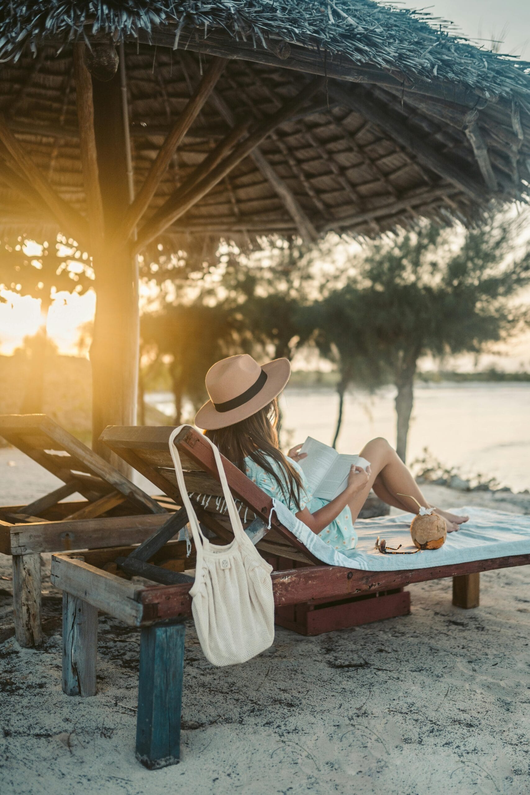 Budget travel tips for Zanzibar 1 A woman reads by the beach under a thatch umbrella in Zanzibar at sunset.