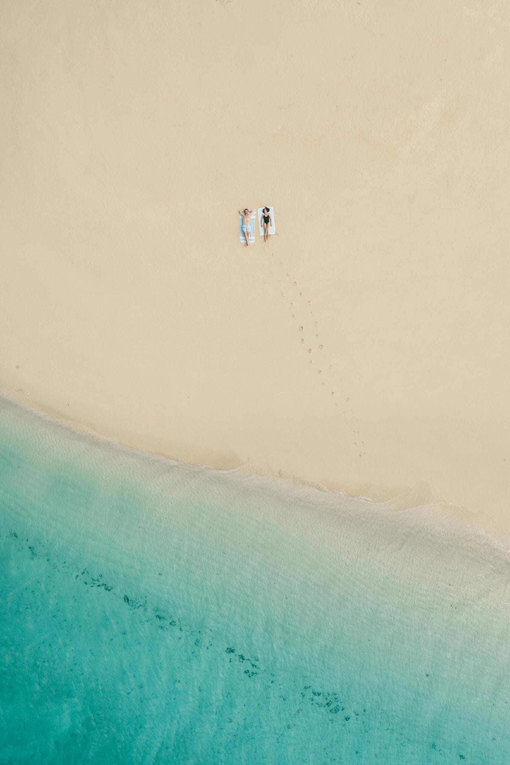 Best beaches in Zanzibar for safaris 1 Peaceful aerial view of a beach in Zanzibar with a couple relaxing on white sand by turquoise waters.