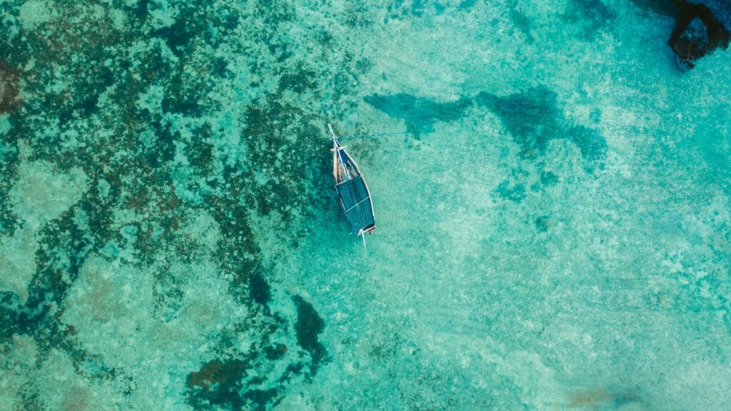 Drone shot of a boat floating in clear turquoise waters of Zanzibar, Tanzania. Serene and scenic top view.