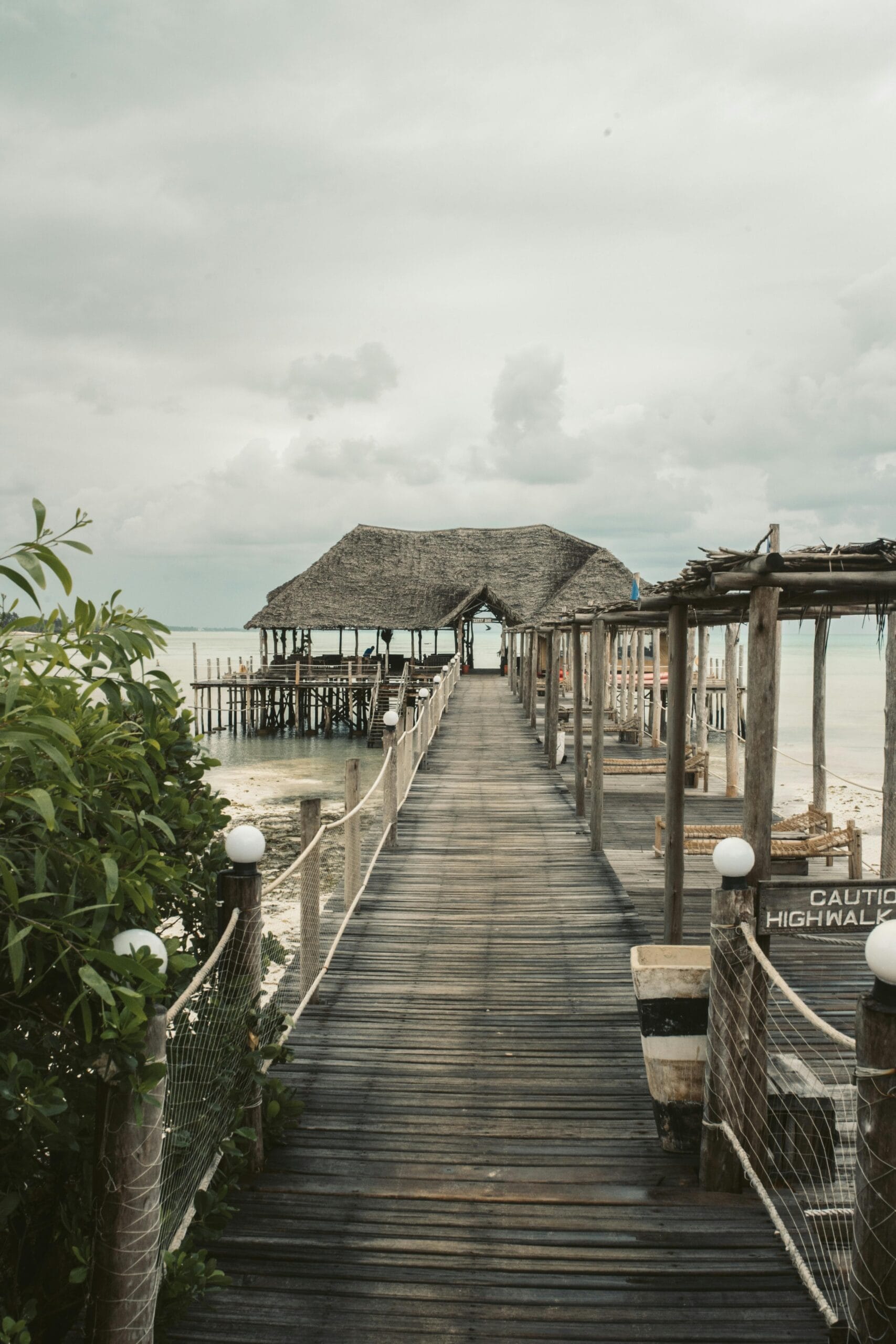 6-Day Family Safari with Zanzibar Beach Add-On: The Ultimate Family Getaway 1 A wooden pier leading to thatched huts over turquoise waters in Zanzibar.