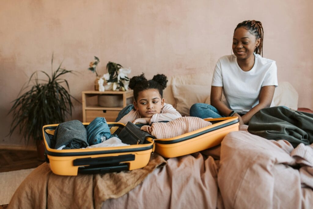 A mother and daughter pack a suitcase on the bed, preparing for travel.