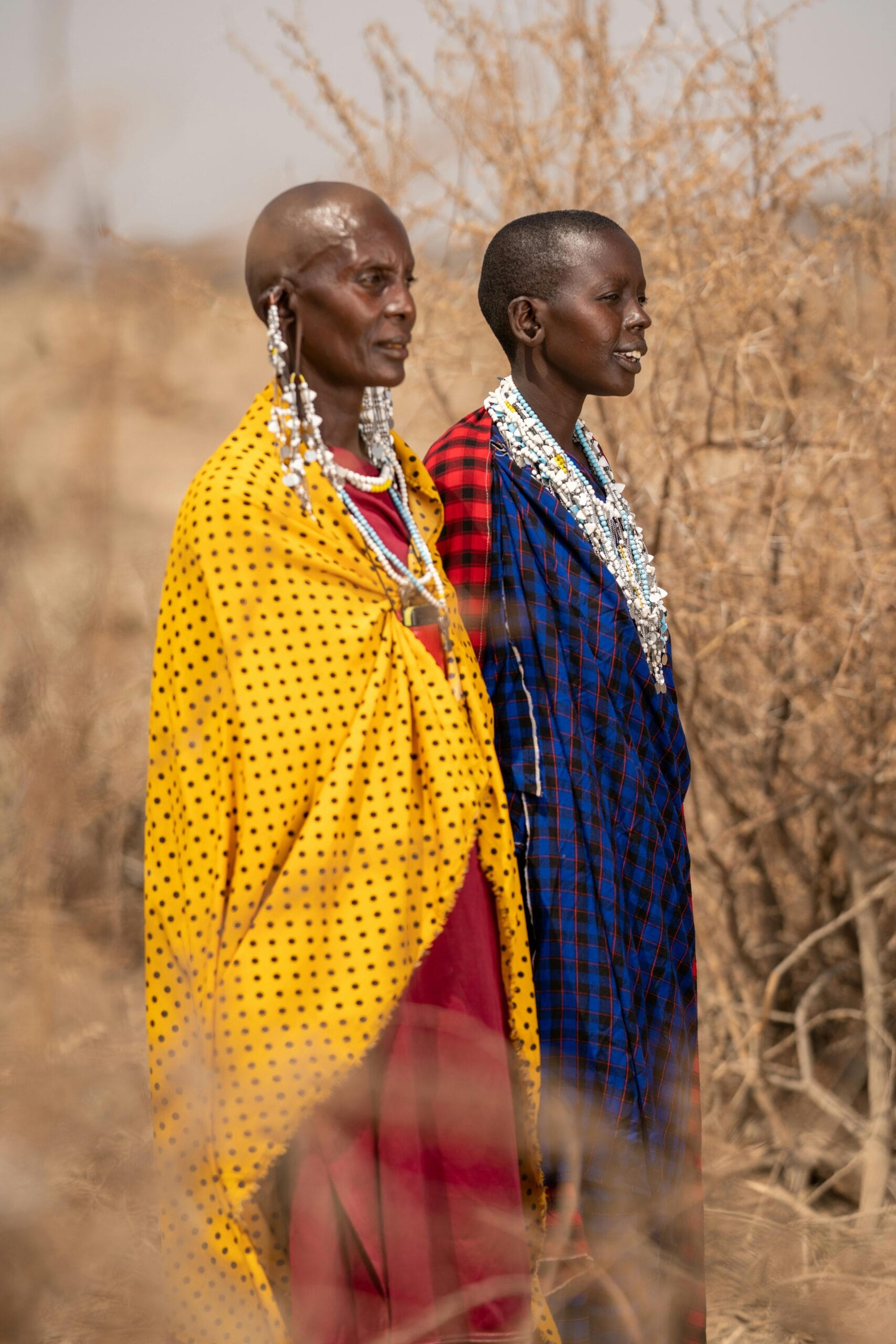 8-Day Family Safari with Maasai Village Experiences 1 Two Maasai women in colorful traditional clothing, standing outdoors in Tanzania.