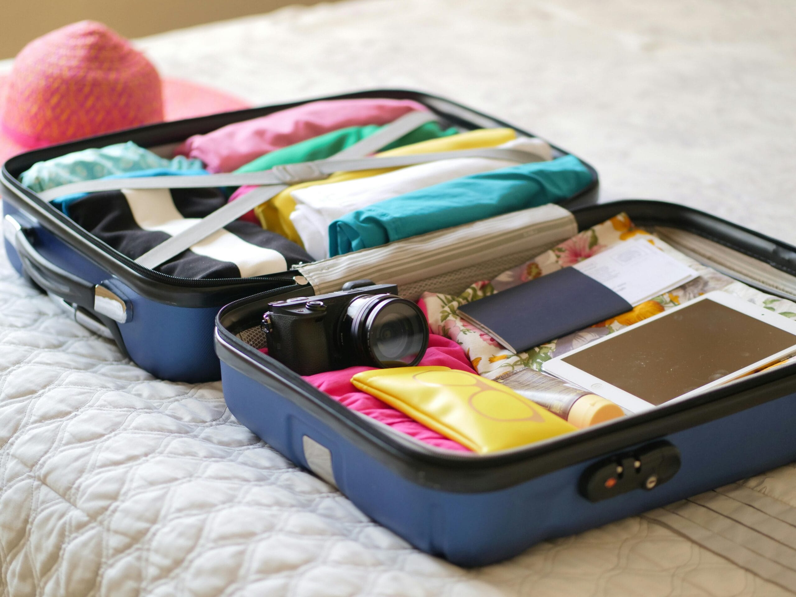 Open suitcase with camera, clothes, and passport, ready for a summer vacation.