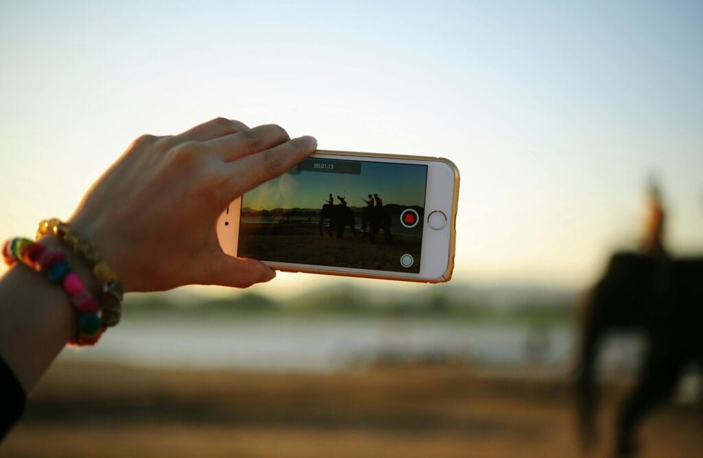 Photography Safari Tips and Guides: Capture the Magic of Africa 1 A colorful bracelet-adorned hand holding a smartphone capturing elephants in the distance.